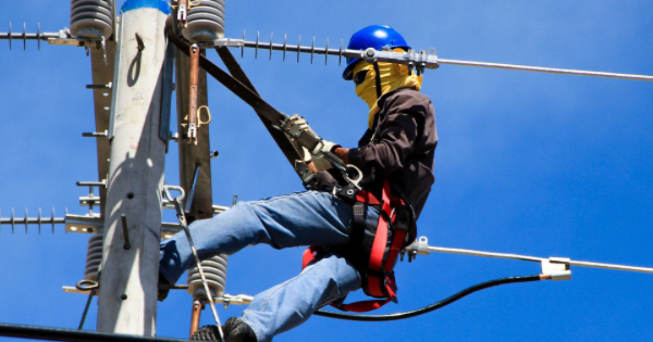 Electrician performing maintenance on power lines, wearing safety gear and harness, emphasizing emergency electrical services.