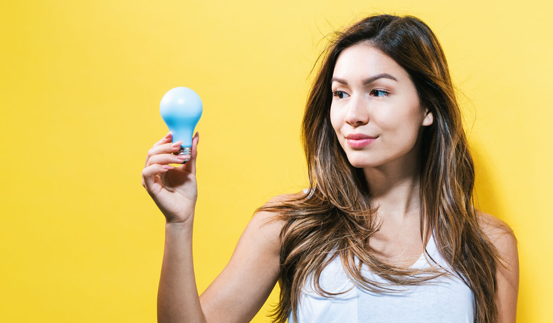 Woman holding a blue light bulb against a bright yellow background, symbolizing household electricity and safety in relation to common electrical myths.