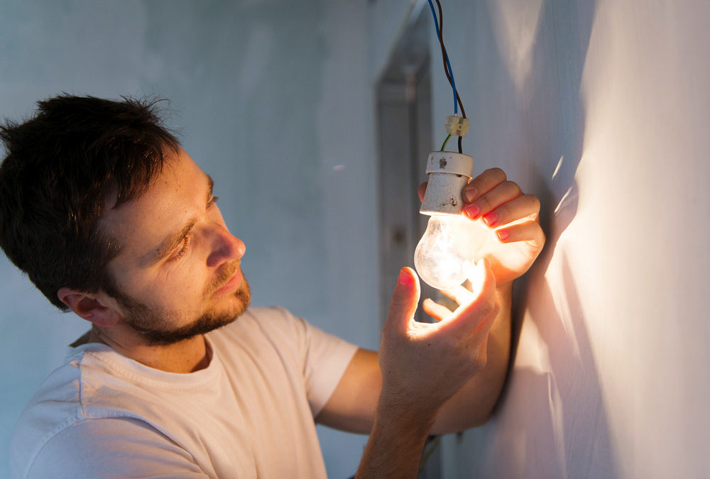Man inspecting a light bulb during electrical repairs, emphasizing the importance of addressing home electrical issues.