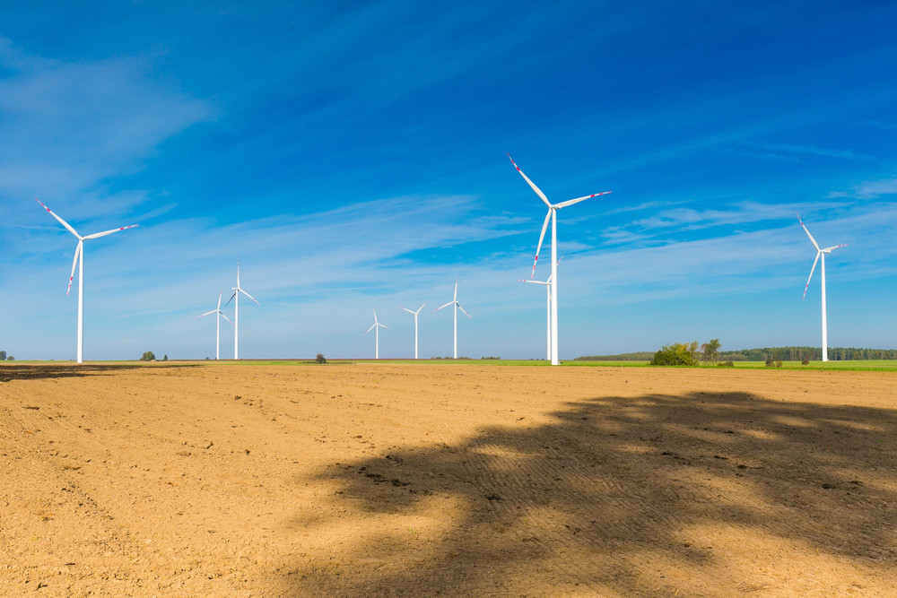 Wind turbines in a clear blue sky over a flat, sandy field, representing sustainable energy solutions and the potential for residential electrical services in the renewable energy sector.
