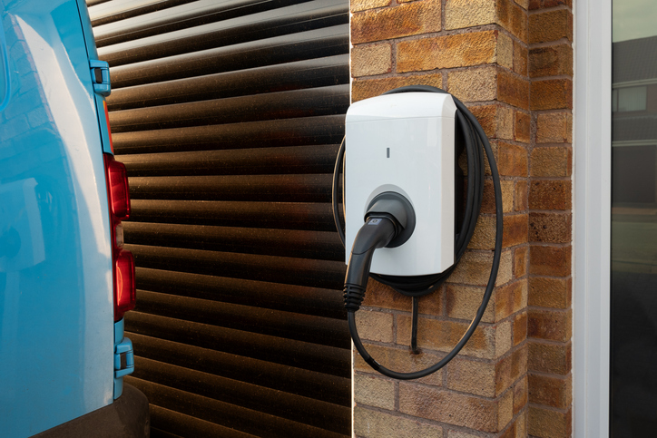 Electric vehicle charging station mounted on a brick wall next to a blue vehicle, illustrating modern electrical upgrades for home value enhancement.