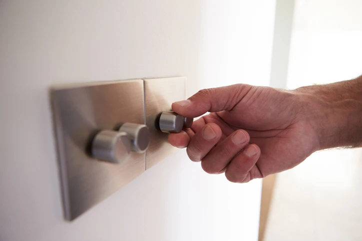 Hand adjusting modern dimmer switch on wall, illustrating Kazar's Electric dimmer switch installation services.