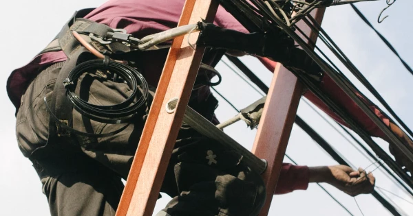 Electrician climbing a wooden ladder, working on electrical wires, emphasizing professional electrical installation and compliance with safety regulations.