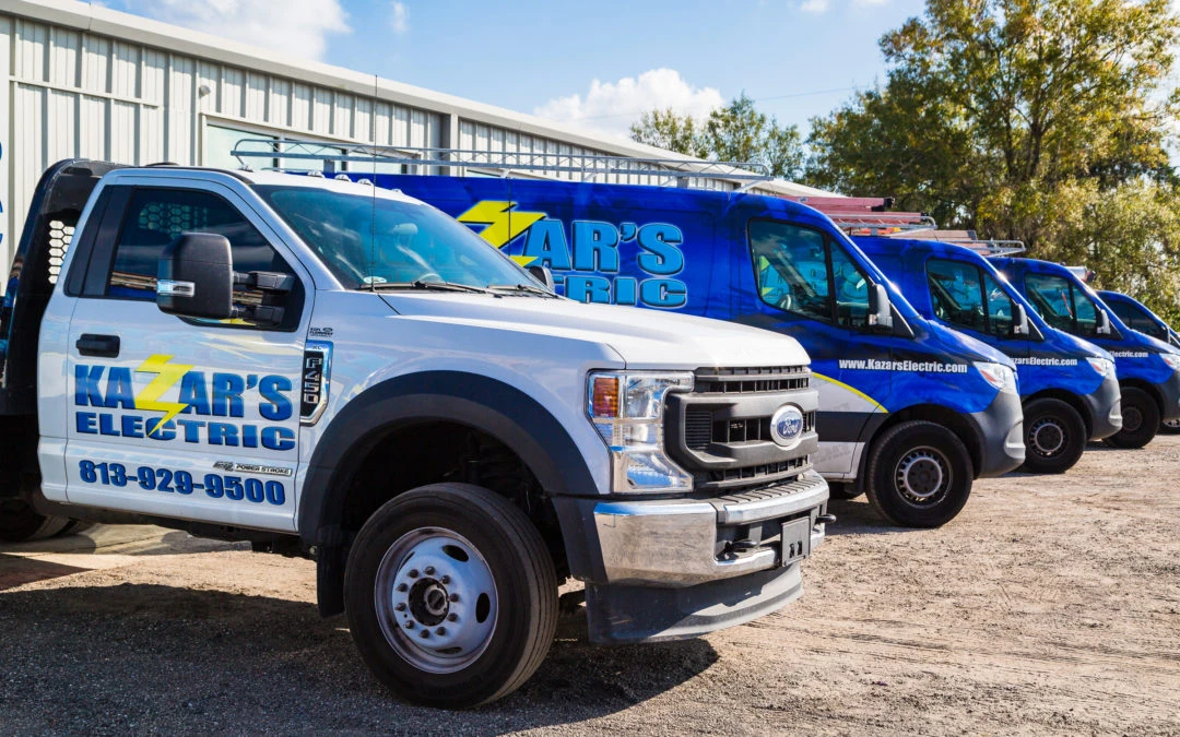 Kazar's Electric service vehicles parked, featuring a prominent white truck and blue vans, showcasing the brand's logo and contact information for professional electrical services.
