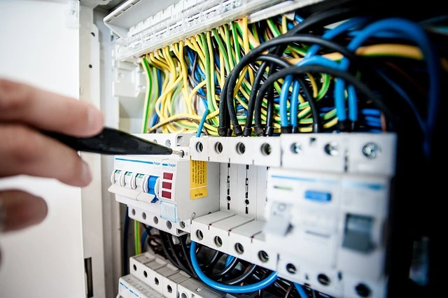 Hand using a tool to adjust circuit breakers in an electrical panel, with colorful wiring visible, illustrating troubleshooting for tripped breakers.