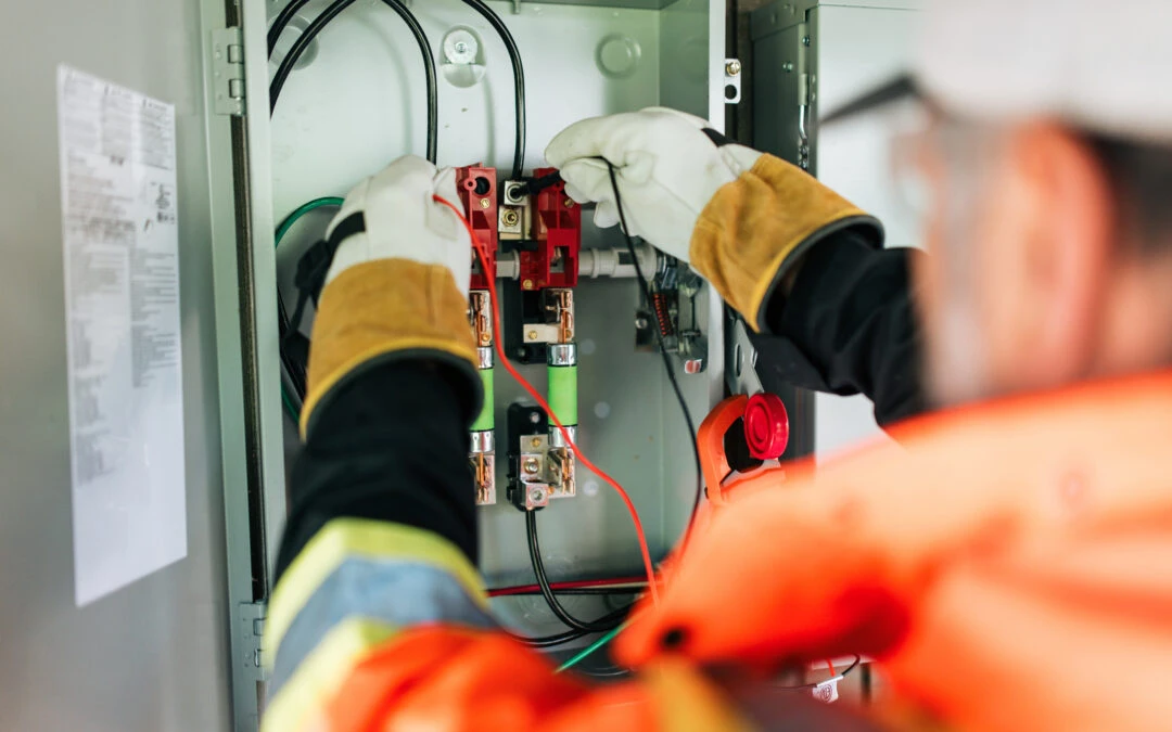 Electrician focused on CATV wiring maintenance, wearing safety gear and working on an electrical panel at Kazar’s Electric.