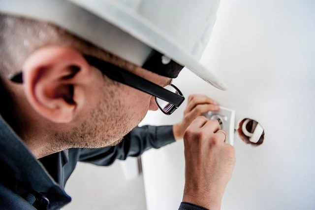 Male technician working on an electrical outlet, highlighting Kazar's Electric's expertise in ceiling fan installations.